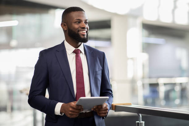 istockphoto-1372138855-612x612 Cheerful young black bearded man manager walking by office building corridor, holding modern digital tablet, using mobile app for business, looking at copy space and smiling, panorama